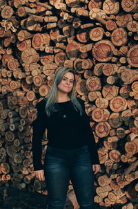 Portrait of woman standing against stacked logs