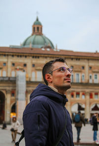 Portrait of young man standing against buildings in city