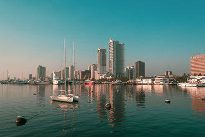 Sailboats in river by buildings against clear sky