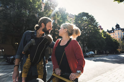 Loving mid adult parents with baby boy walking on sidewalk in city