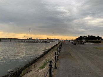 View of road by river against cloudy sky