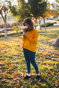 Curly young girl in yellow sweater on the grass with autumn bouquet of dry leaves and flowers