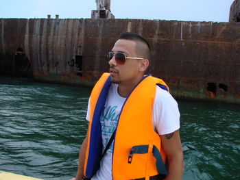 Young man in life jacket standing against river