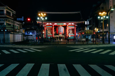 Illuminated road by buildings in city at night