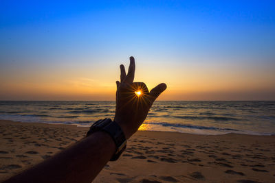 Cropped hand of woman gesturing ok sign at beach against sky