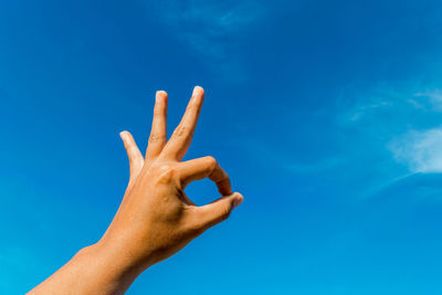 Cropped hand gesturing ok sign against blue sky