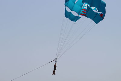 Low angle view of people parasailing against clear sky