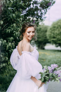 Beautiful bride in a wedding dress walks in a blooming apple-tree park in spring