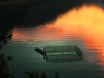 Mid distant view of man by fishing net in lake during sunset