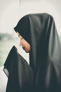 Side view of woman wearing hijab praying against sky