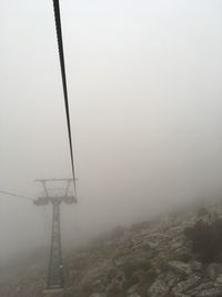 Electricity pylon in foggy weather against sky during winter