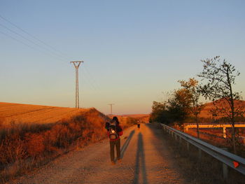 Rear view of man walking on road against clear sky