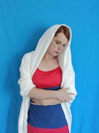 Thoughtful woman standing against blue wall