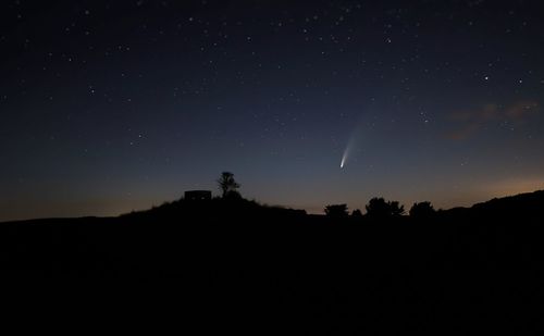 Silhouette landscape against sky at night with meteor