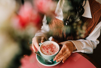 A young smiling woman enjoys a coffee drink while holding a mug while sitting in a cafe