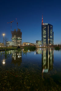 Illuminated modern buildings in city against sky at night