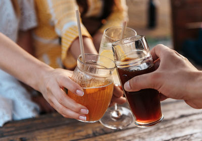 Close-up photo of friends clinking glasses, having drinks in bar outdoor in summer