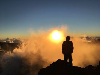 Rear view of silhouette man standing on rock against sky during sunset