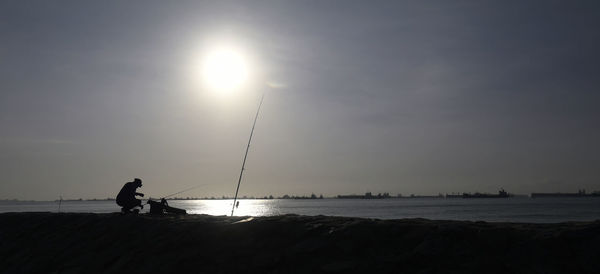 Silhouette man fishing in sea against sky