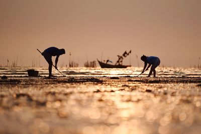 People fishing in sea against sky during sunset