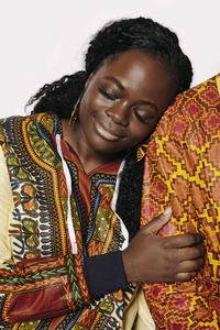 Dreamy curvy woman in traditional african clothes hugging an anonymous person standing on white background in studio