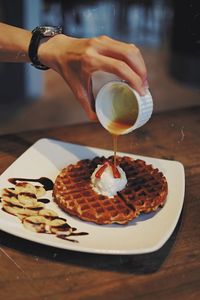 Cropped hand of man pouring caramel on sweet food at table
