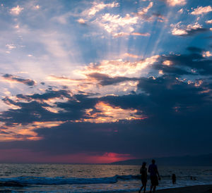 Silhouette people at beach against sky during sunset