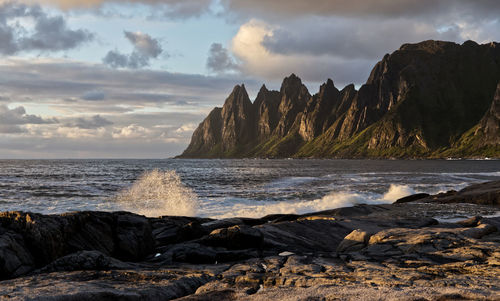 Scenic view of sea and a dramatic mountain range against sky during sunset