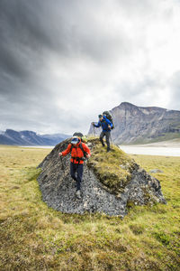 Backpackers hiking over large boulder in akshayak pass.