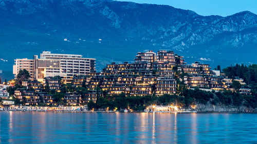 Illuminated buildings by sea against sky in city