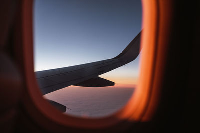 Through window of wing of airplane flying over fluffy clouds in sunset blue sky