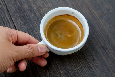 Cropped hand of person holding fresh espresso cup on table