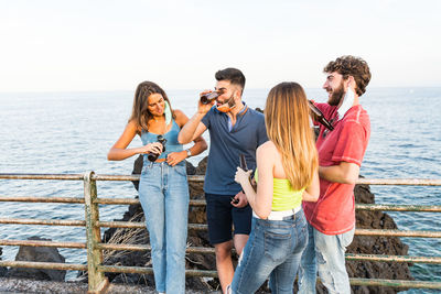 Friends drinking beer while standing by railing against sea