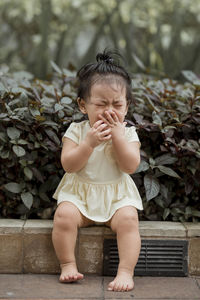 Crying cute girl while sitting on sidewalk against plants