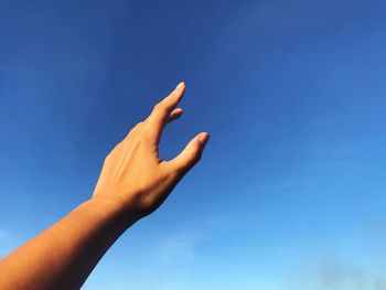 Low angle view of hand against blue sky