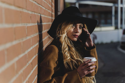 Young woman wearing hat while standing against wall