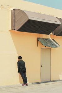 Rear view of man walking on footpath against building