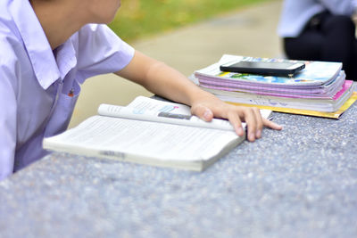 Midsection of teenage student reading book at table