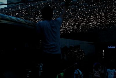 Rear view of man with arms raised at night