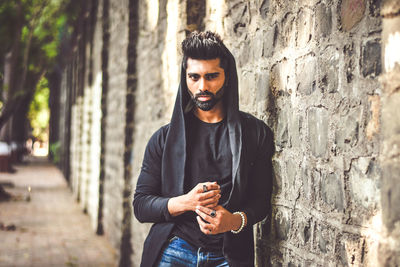 Portrait of young man standing by wall in city
