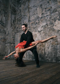 Full length of man and woman dancing on floor against wall