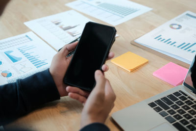 Cropped hands of businessman using smart phone while working at table in office