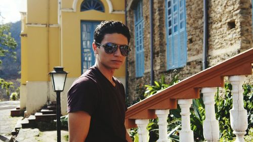 Young man wearing sunglasses standing by railing against monastery