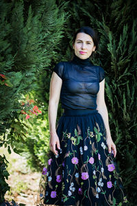 A young pretty woman in black clothes is standing near a bush