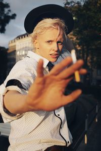 Portrait of young woman holding hat standing outdoors