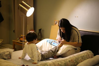 Mother cutting toenails of son on bed at home