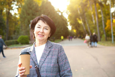 Portrait of smiling woman standing against trees in city