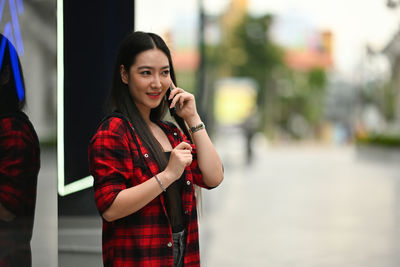 Young woman holding camera while standing against city in background