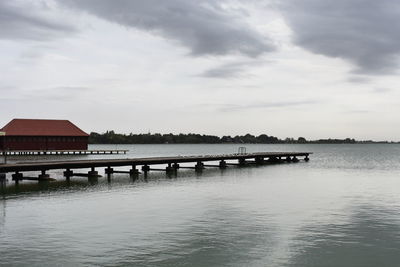 Pier over lake and houses against sky