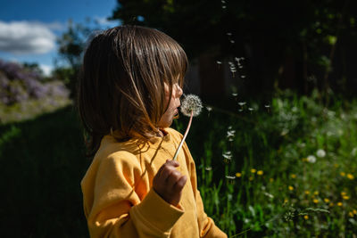 Child in yellow clothes blowing a flower